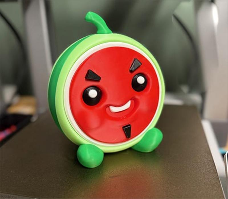 Stylized watermelon character container with a smiling face, black triangular accents, and green rind, standing on sm...