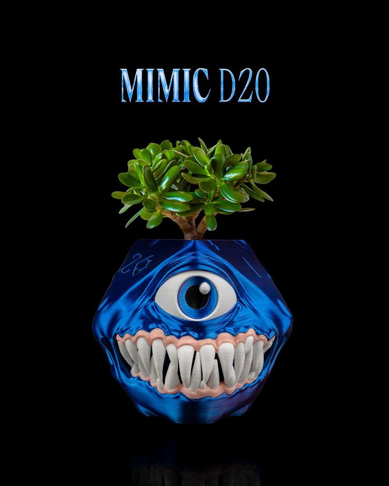 A metallic blue D20-shaped planter with a large eye and sharp teeth, holding a small succulent plant. The planter res...