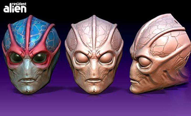 Three views of a 3D model of an alien mask. The left mask is colored blue and red with large green eyes. The middle a...