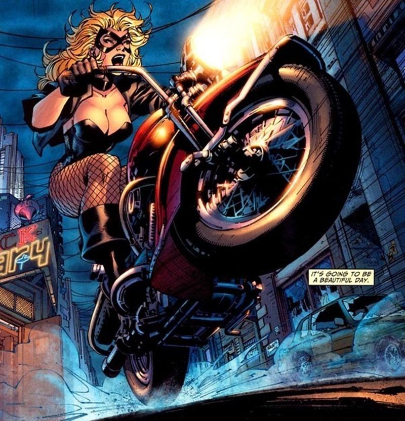Black Canary riding a motorcycle, performing a wheelie in a city street at night. She wears a black costume with fish...