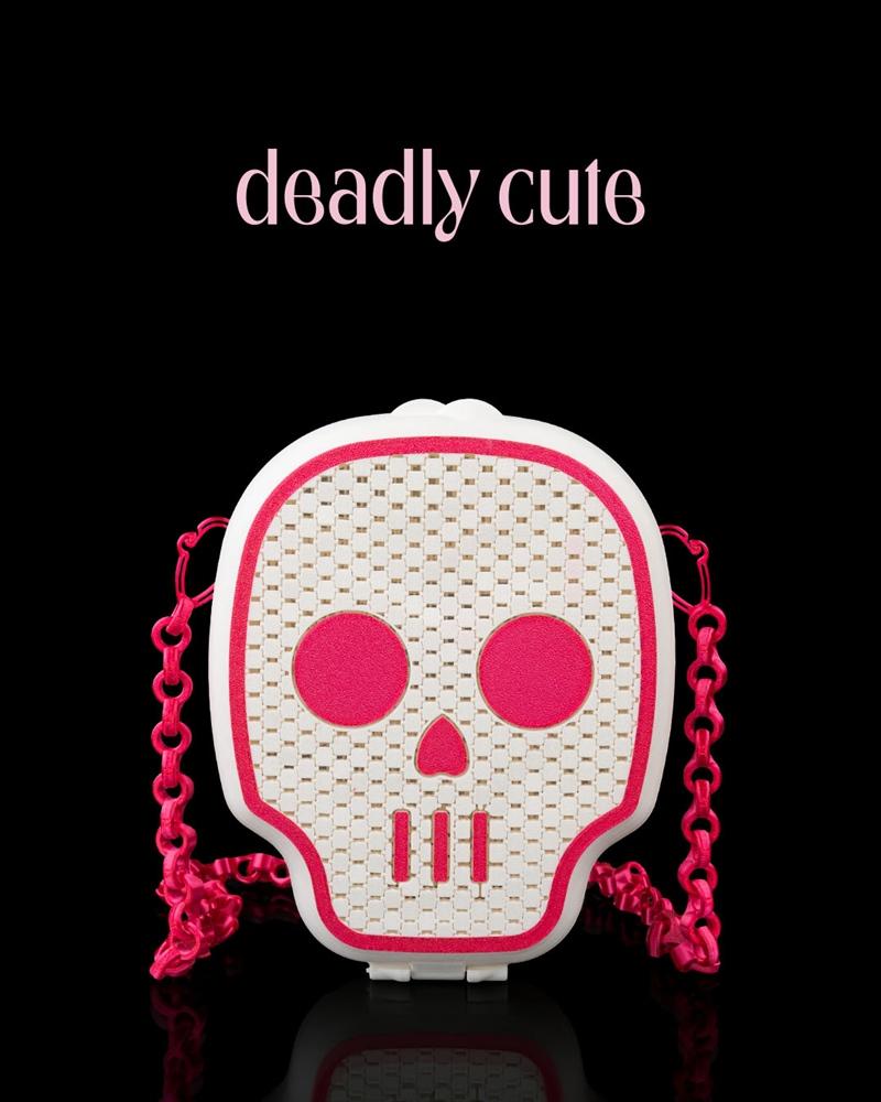 White skull-shaped bag with pink accents and a pink chain strap, featuring a woven texture and the text "deadly...