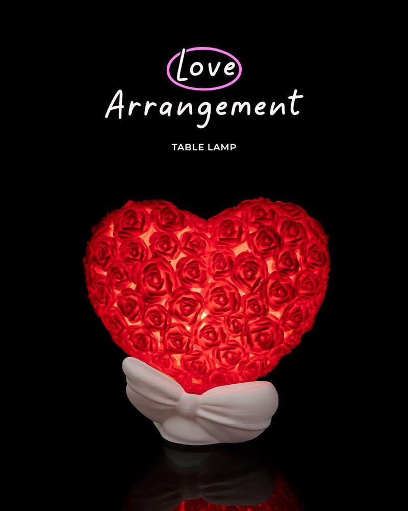 Heart-shaped table lamp covered in red roses, with a white bow-shaped base, illuminated from within.
