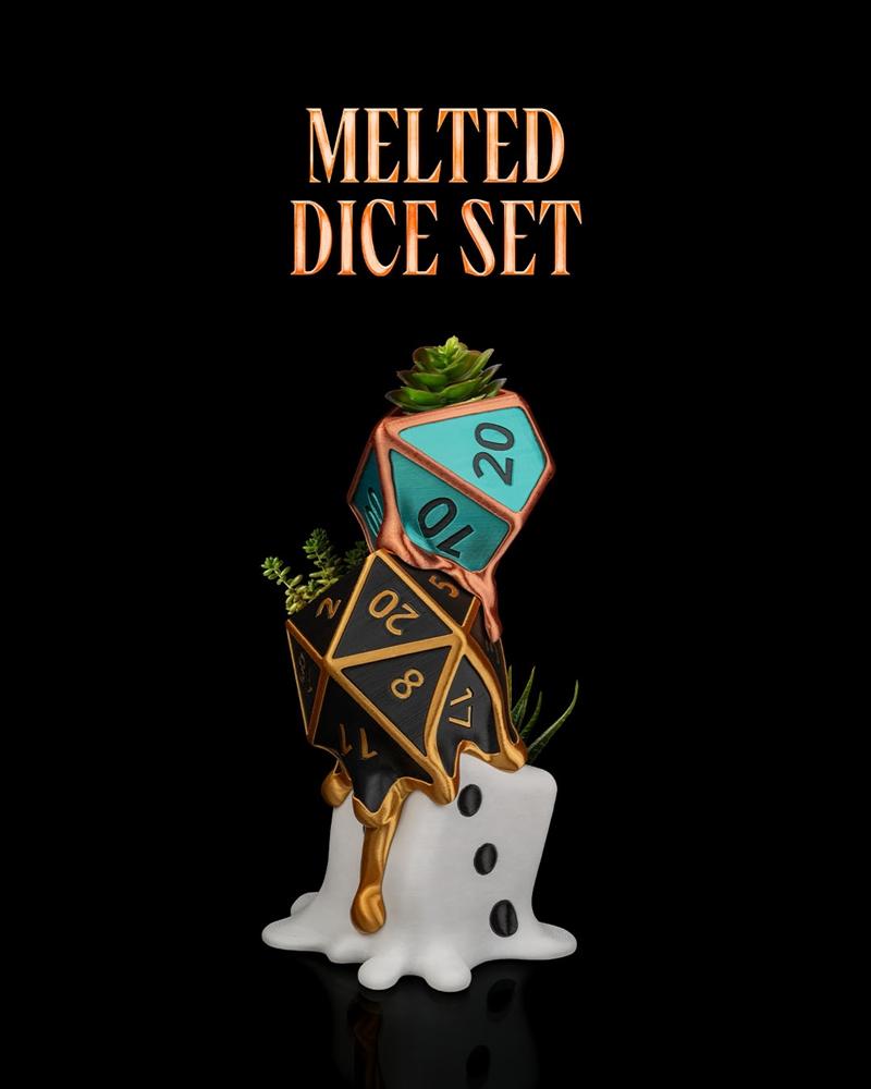A teal and black polyhedral dice set appearing to melt over a white base, with a succulent plant on top and greenery...