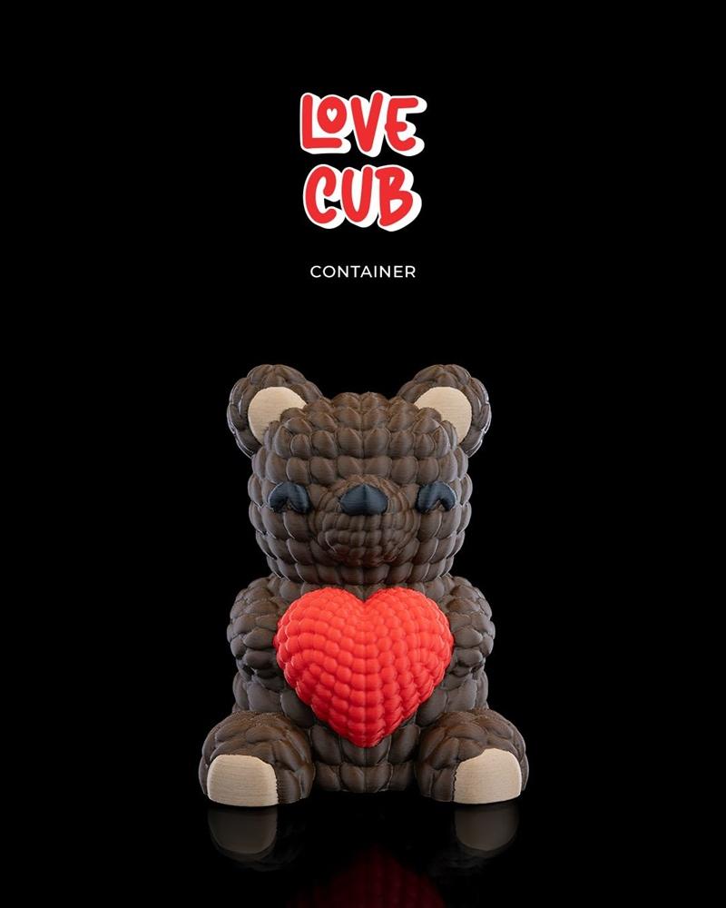 3D printable model of a brown, textured teddy bear figure holding a large red heart. Text above reads "LOVE CUB...