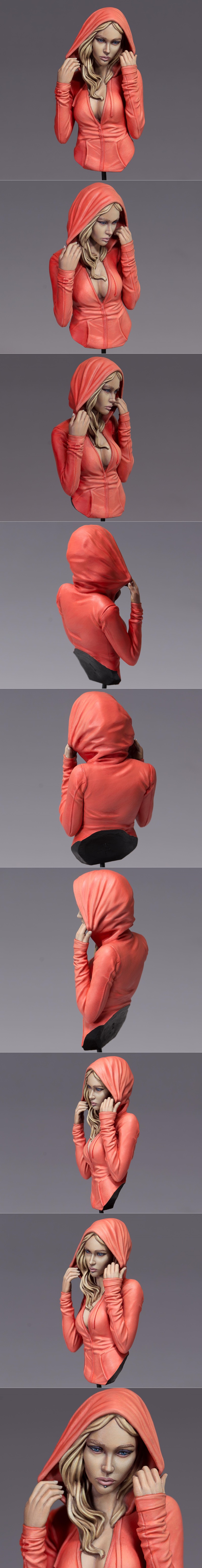 Bust of a blonde woman with blue eyes and a lip piercing, wearing an unzipped coral hoodie and adjusting the hood.