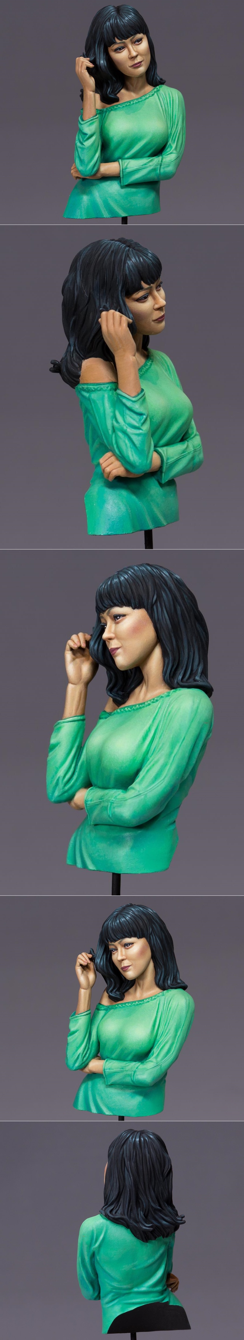 Bust of a woman with dark hair, wearing a green off-the-shoulder top, with one hand touching her hair and the other c...