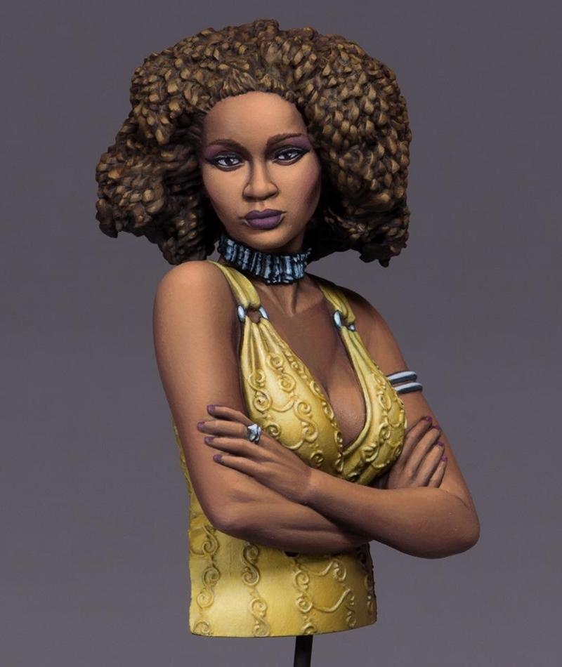 Bust of a woman with a large, curly brown afro hairstyle, wearing a yellow, patterned halter top and a dark, textured...