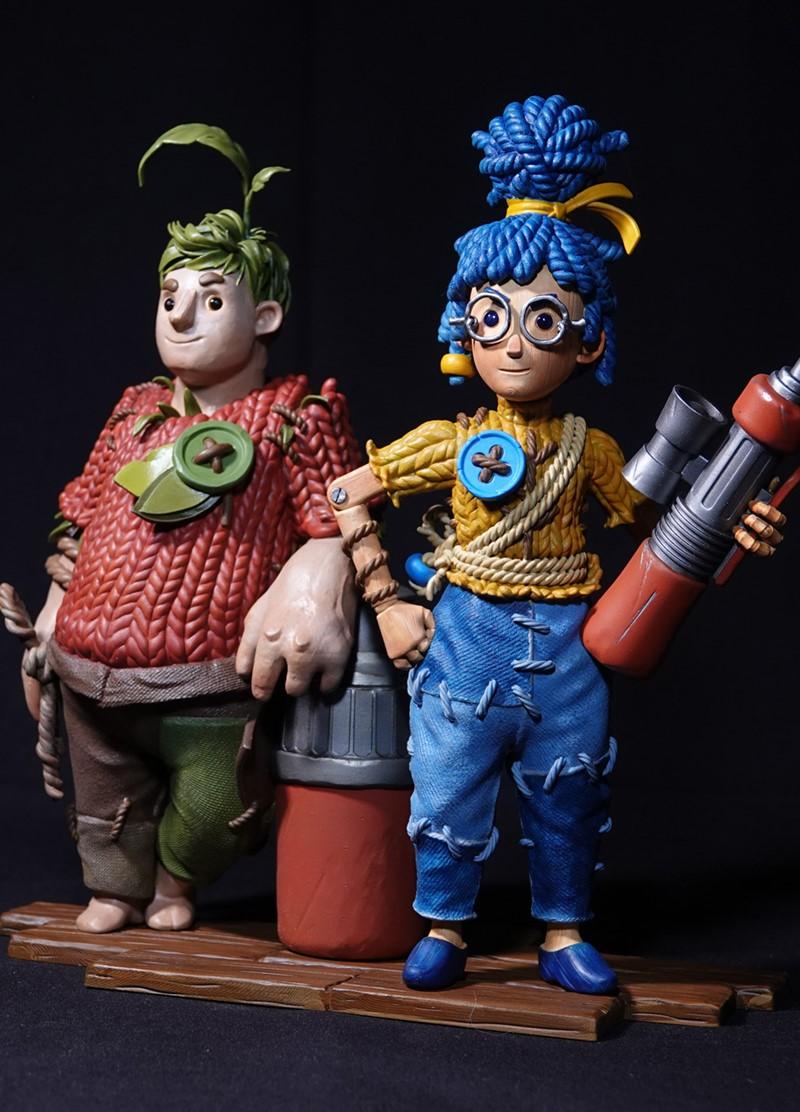 3D printed figures of Cody and May from It Takes Two, rendered in a claymation style. Cody wears a red knitted sweate...